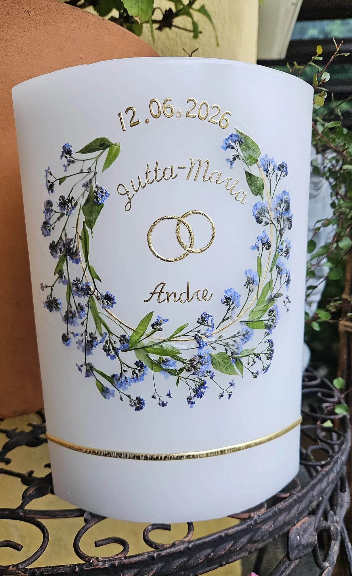 Hochzeitskerze mit blauem Blütenkranz und Ringen