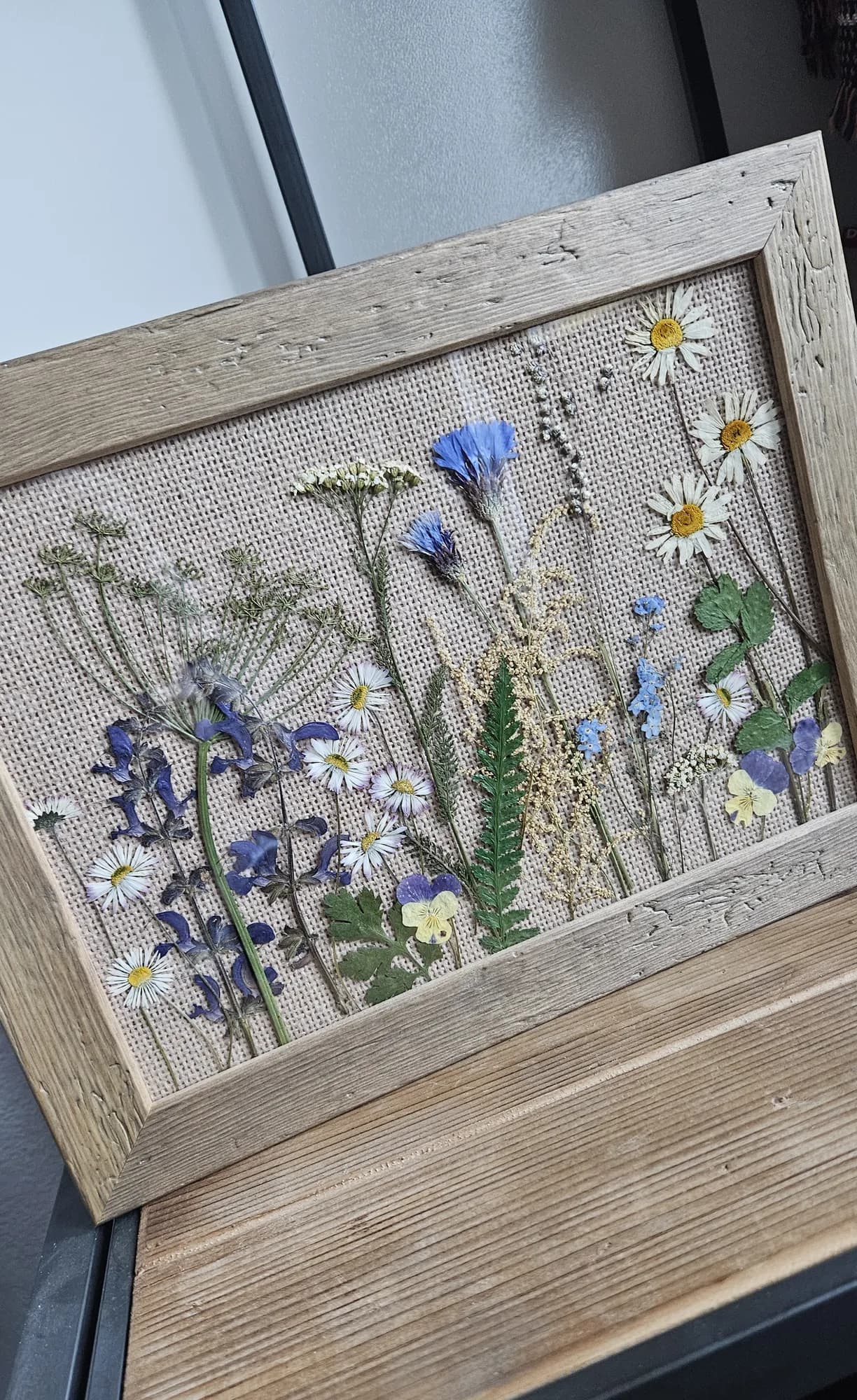 Trockenblumenbild mit Kornblumen, Margeriten und Vergissmeinnicht auf Jute in einem rustikalen Holzrahmen