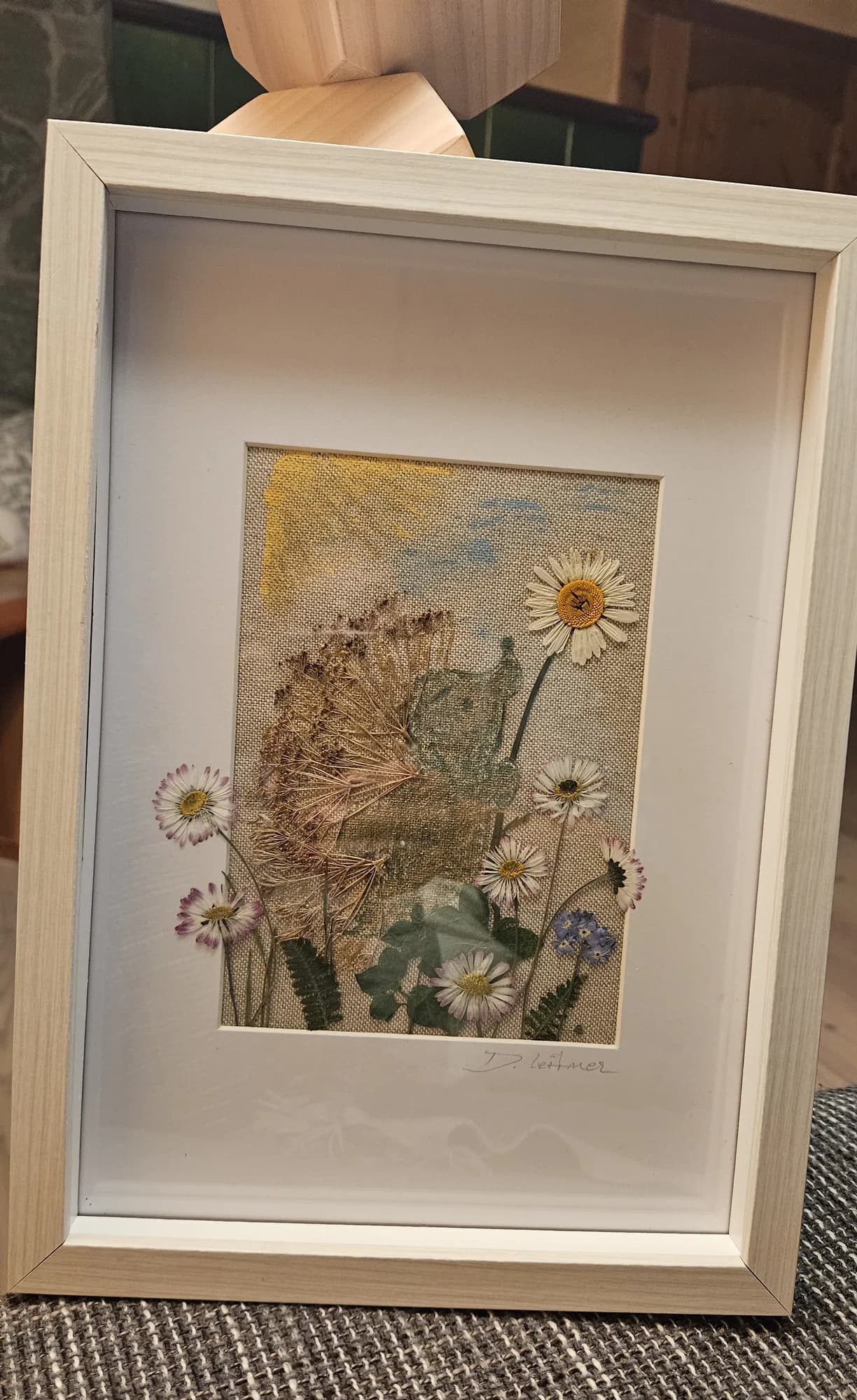 Gerahmtes Bild mit Gänseblümchen und Pusteblume vor gemaltem Himmel auf Leinen