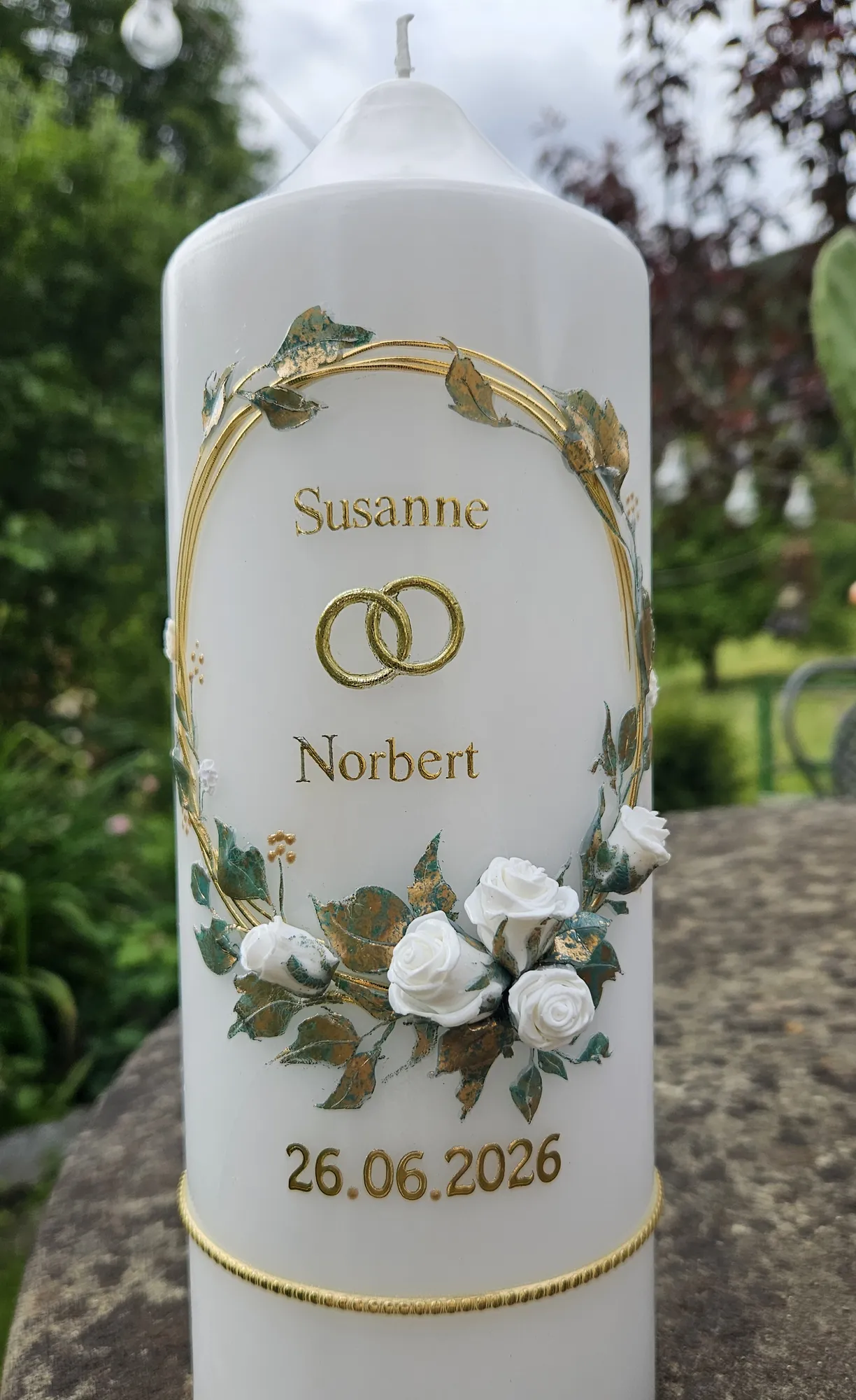 Weiße Hochzeitskerze mit goldenem Bogen, Trauringen und weißen Rosen