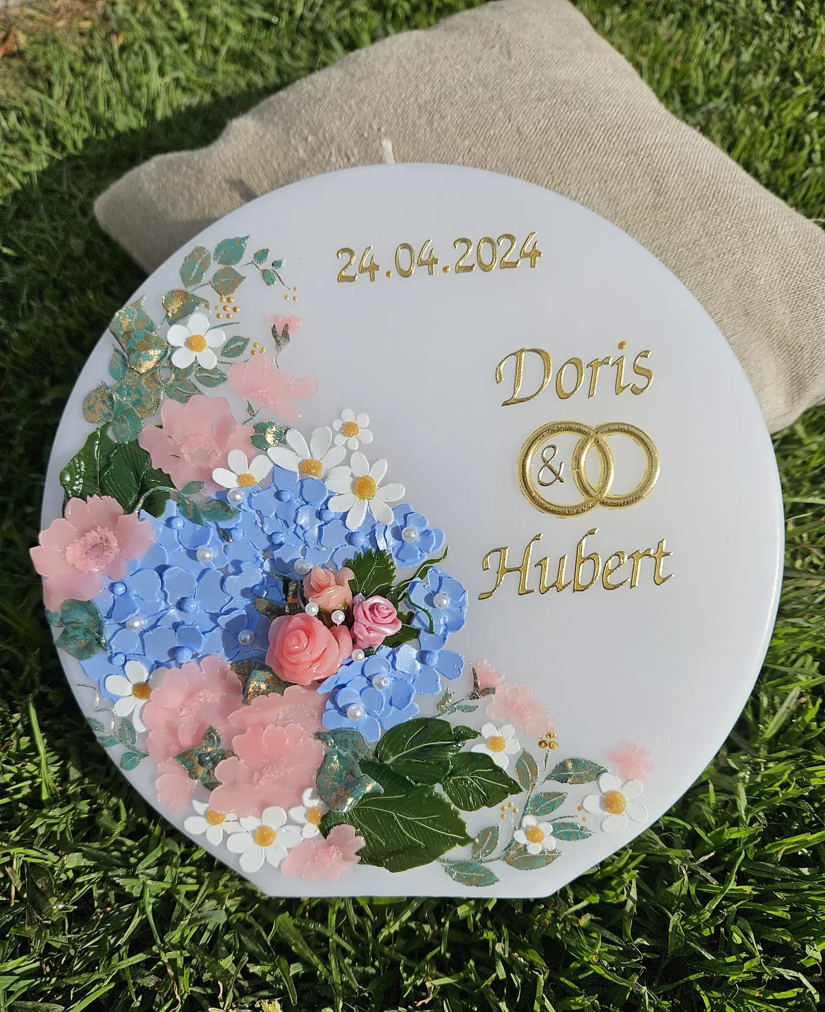 Runde Hochzeitskerze mit blauen Hortensien, rosa Rosen und goldenen Ringen