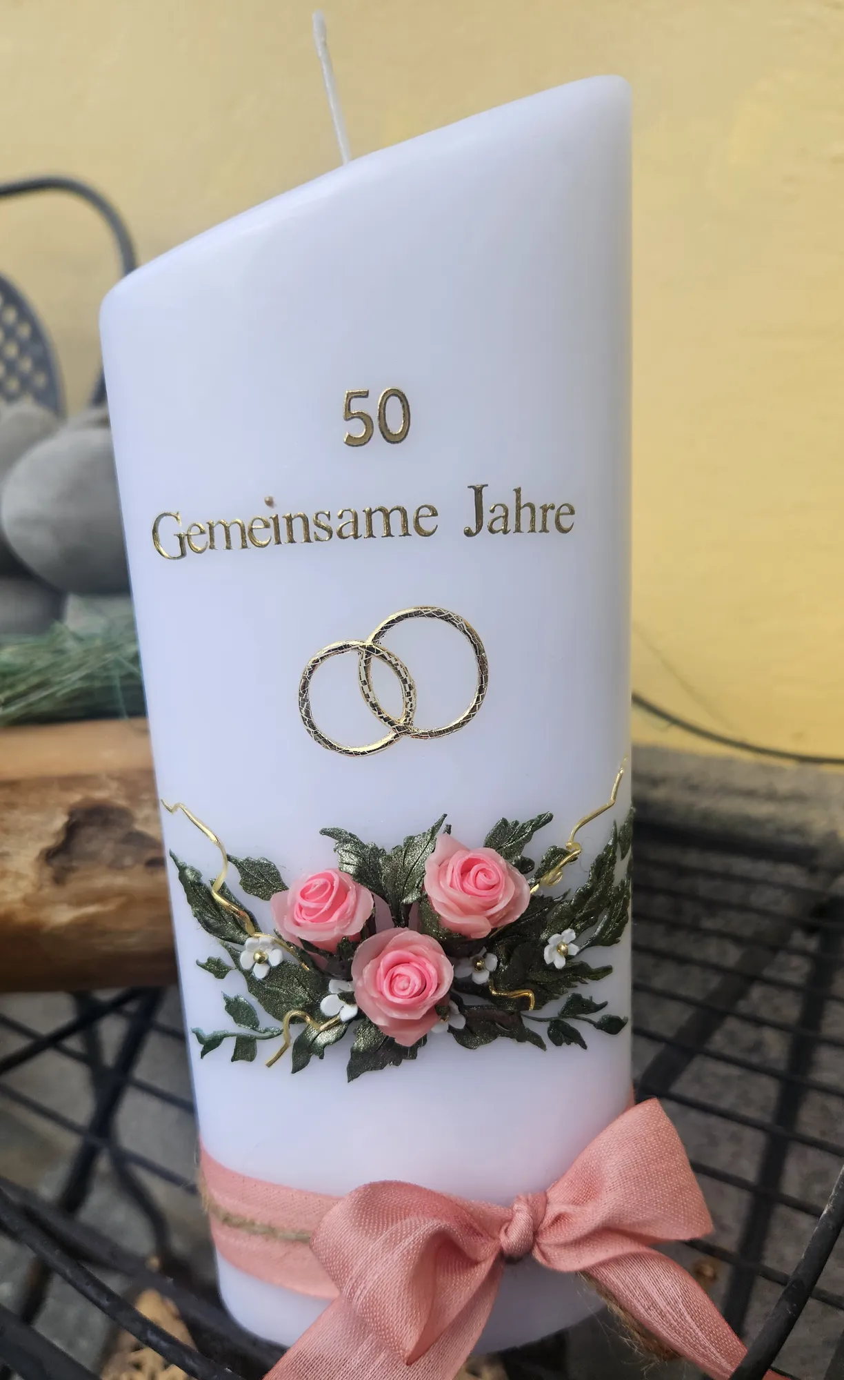 Weiße Jubiläumskerze mit goldenen Ringen, der Zahl 50 und rosa Rosen