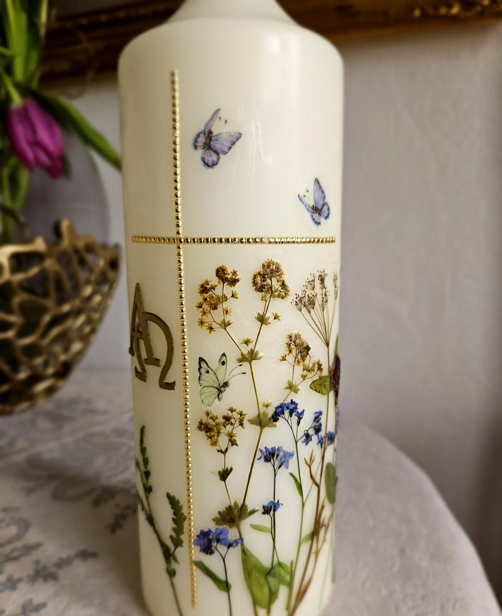 Gedenkkerze mit gepressten Wiesenblumen, Schmetterlingen und goldenem Kreuz mit Alpha und Omega
