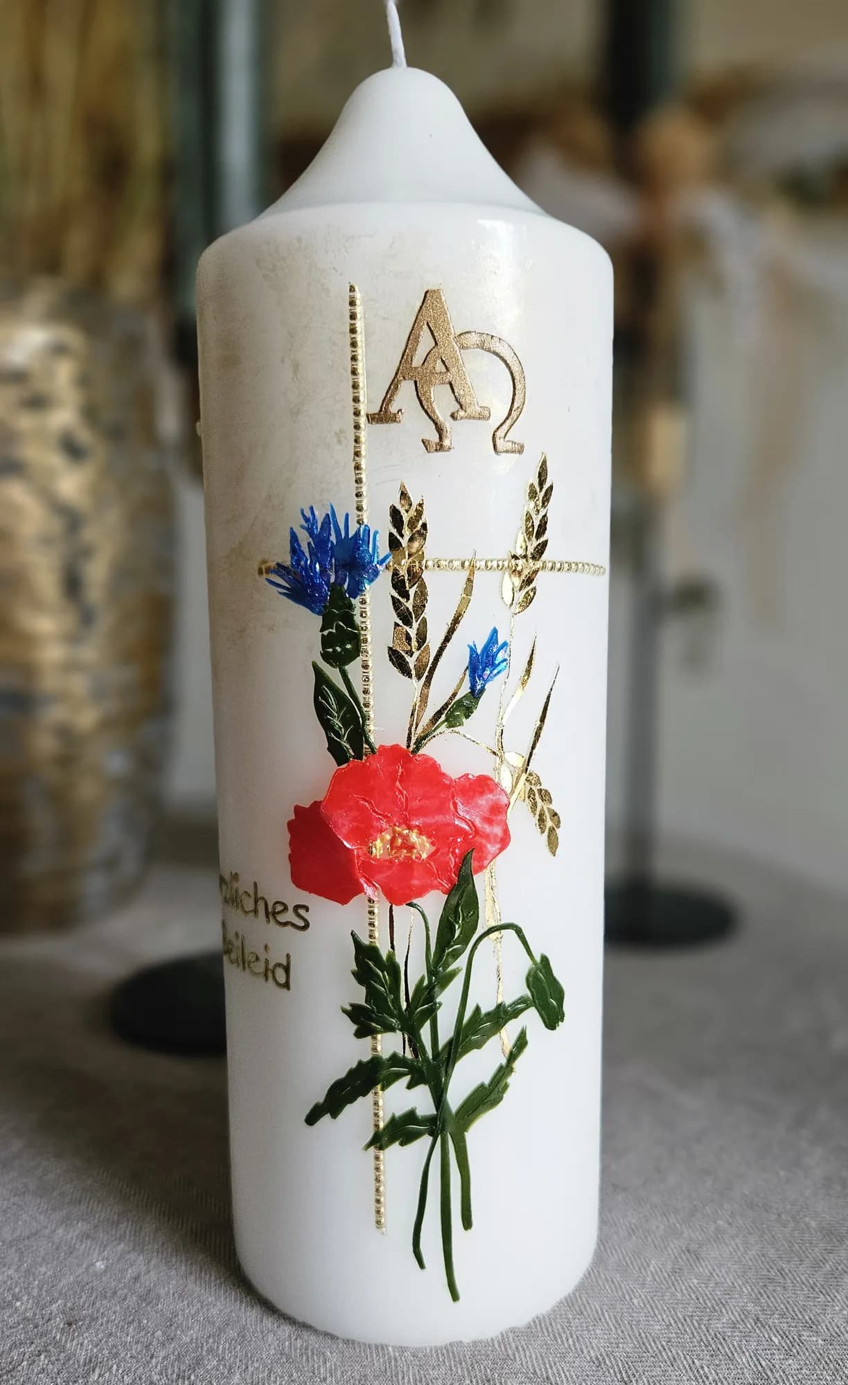 Weiße Trauerkerze mit blauer Kornblume, rotem Mohn, goldenen Ähren sowie Alpha und Omega