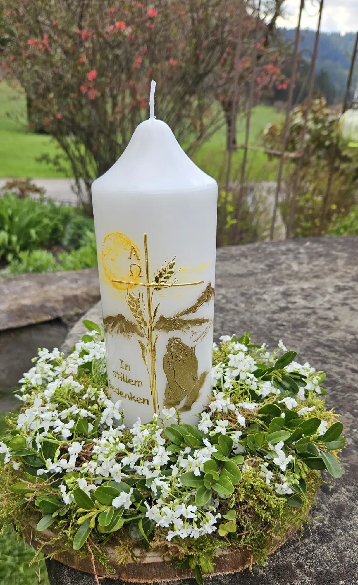 Gedenkkerze mit goldenen Ähren und betenden Händen in einem Kranz aus weißen Blüten